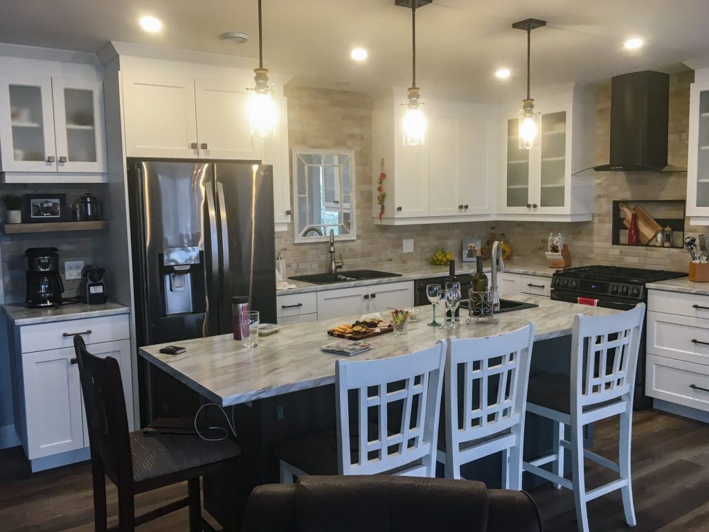 Open concept modern kitchen with large stone island, natural stone backsplash, shaker cabinets, and high-end stainless appliances with dedicated coffee bar.