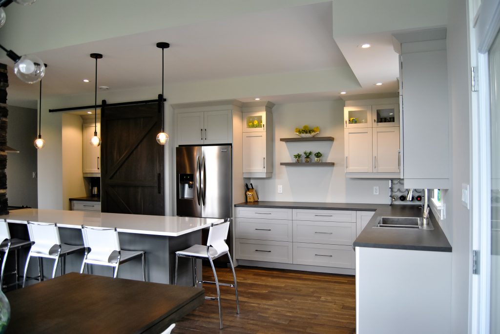 New construction custom white kitchen with grey countertops, recessed lighting, and an enclosed pantry with a dark wood sliding barn door.