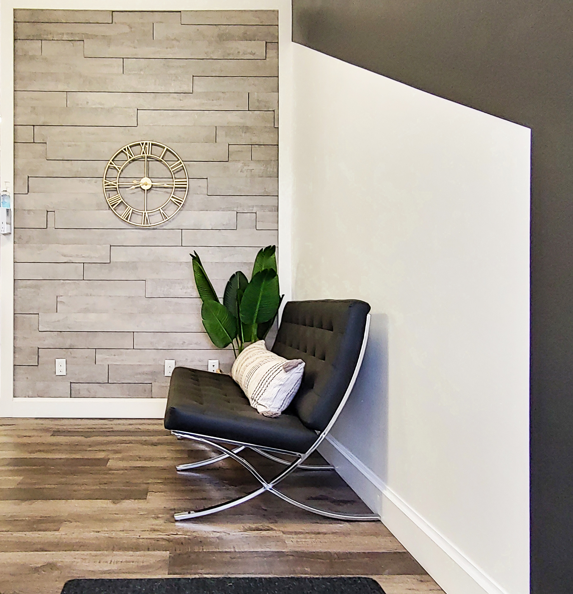 New front office space with wide plank hardwood floors, stone tile walls, potted palm plant, and a modern grey bench.