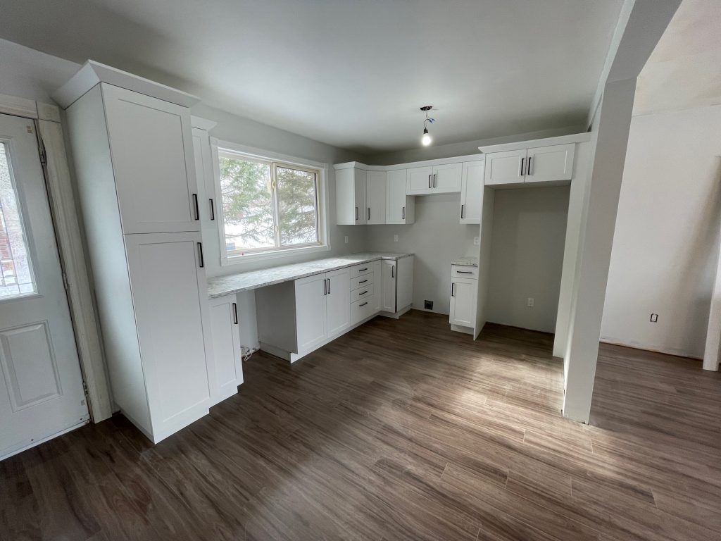 Newly renovated kitchen with all white cabinets and stainless hardware. Spaces for appliances are empty.